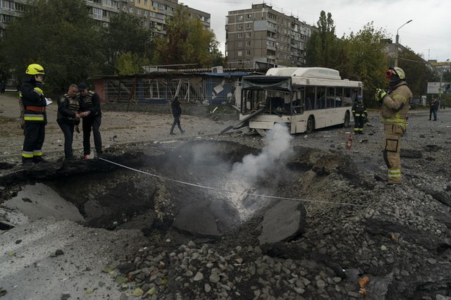 Украински пожарникари и полицаи се отзовават на мястото на екплозия, издълбала кратер на улица, след руски обстрел по град Днепър на 10 октомври 2022 г. Снимка: АП