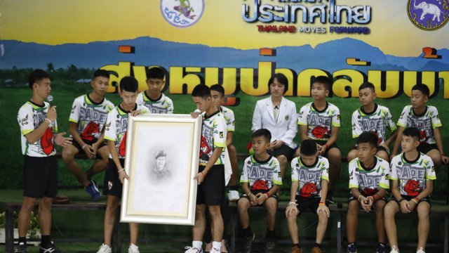 Треньорът на момчетата (вляво) и децата показват портрет на загиналия по време на спасителната операция водолаз Саман Гунан. © Associated Press