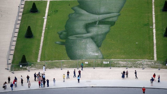 Туристи разглеждат огромната творба на уличния артист Saype, която е направена с биоразградима боя върху тревата в парка "Марсово поле" в Париж. © Reuters